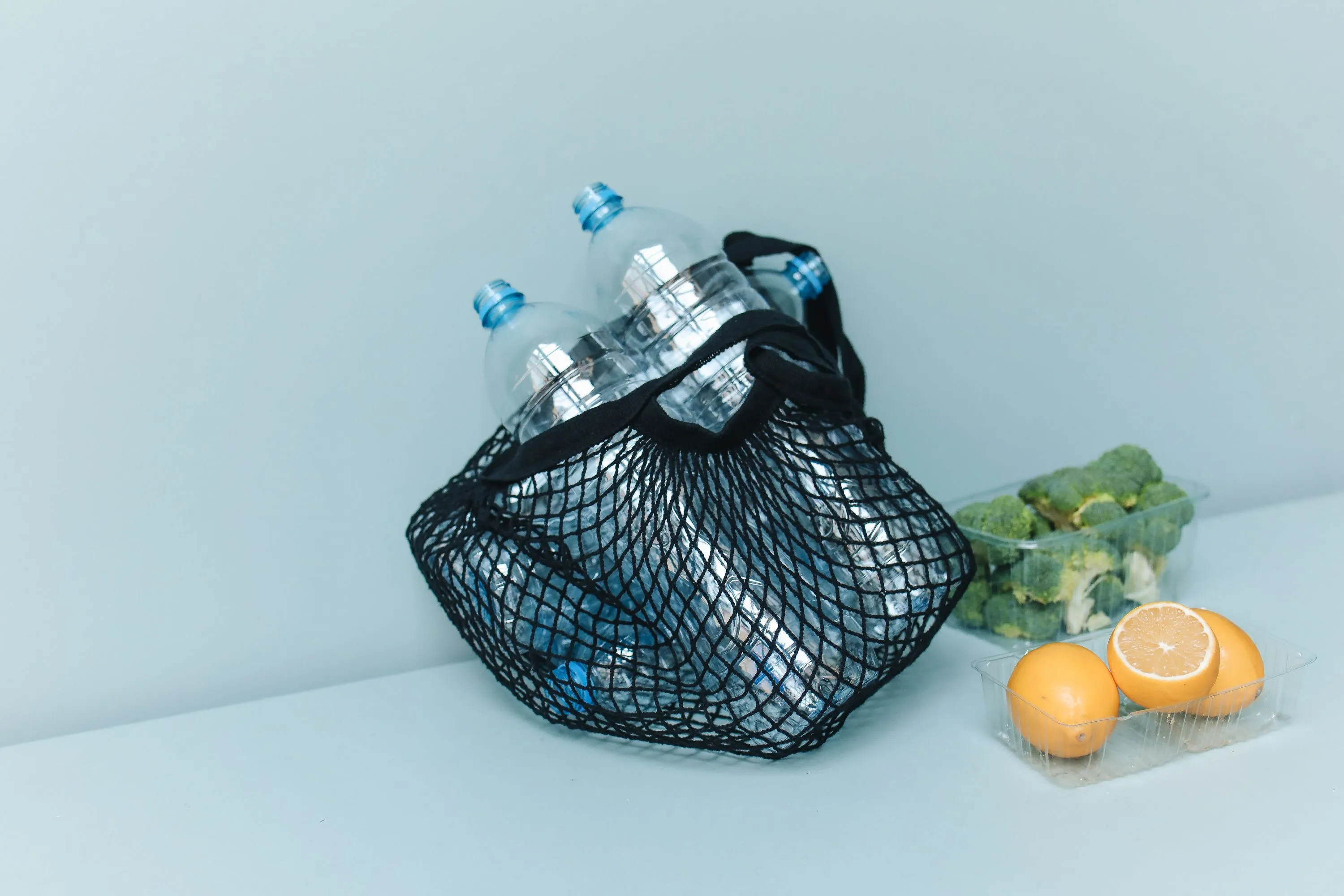 Reusable mesh shopping bag holding plastic bottles and groceries